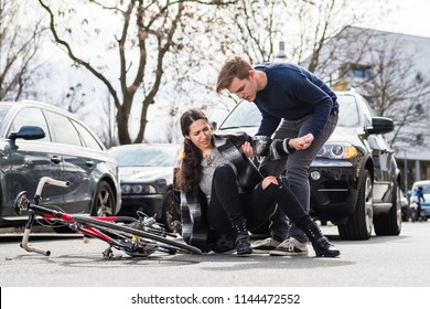 Reliable young man helping an injured woman while waiting for the ambulance after bicycle accident on city street - Powered by Shutterstock