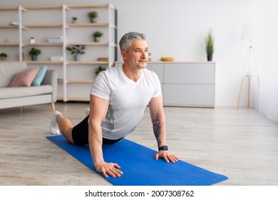 Relief lower back pain. Mature man doing sphinx cobra pose or upward-facing dog asana stretching back muscles, excercising in living room on yoga mat, copy space