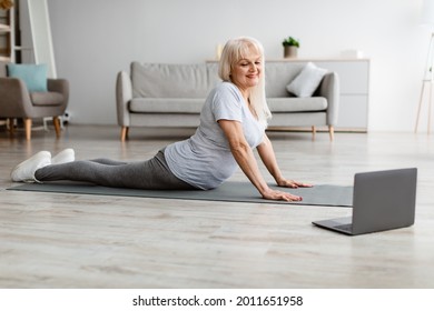 Relief Lower Back Pain. Smiling Mature Woman Doing Sphinx Cobra Pose Or Upward-Facing Dog Asana Stretching Muscles Practicing Pilates, Excercising In Living Room On Yoga Mat, Using Laptop - Powered by Shutterstock