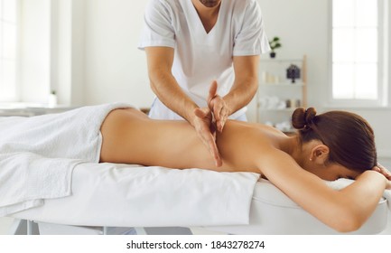 Relieving back muscle tension. Male masseur massaging young woman using Tapotement movements aka chopping, tapping or hacking technique during Swedish massage therapy in spa salon or wellness center