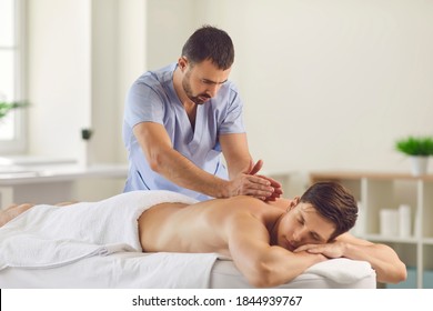 Relieving back muscle tension. Professional masseur massaging young man's back using Tapotement or chopping, tapping or hacking technique during Swedish massage therapy in spa salon or wellness center