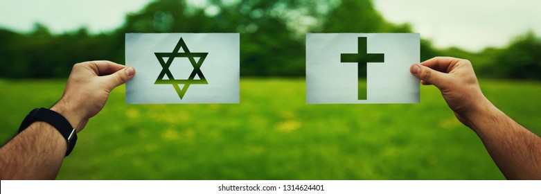 Religion conflicts as global issue concept. Two hands holding different faith symbols, Judaism vs Christianity belief over green field nature. Relations between different people doctrines and cult.