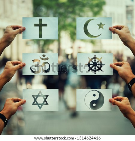 Religion conflicts as global issue concept. Human hands holding different paper with faith symbols over crowded street scene. Relations between different people doctrines and beliefs, social problem.