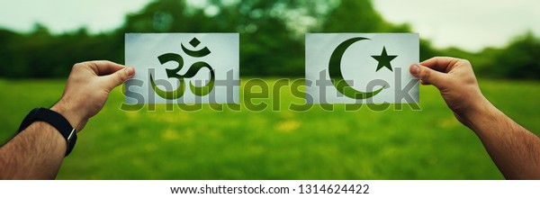 Religion conflicts as global issue concept. Two\
hands holding different faith symbols, Islam vs Hinduism belief\
over green field nature. Relationship between different people\
doctrines and cult.