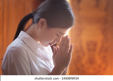 Religious Asian buddhist woman praying. Female buddhist disciple meditating, chanting mantra with prayer hand to the statue of lord Buddha in temple hall; Southeast Asian Dheravada Buddhism style