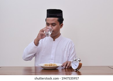 Religious Asian man in koko shirt or white muslim shirt and black cap drinking water while eating noodle for suhoor to be strong during fasting from dawn until dusk in ramadan month - Powered by Shutterstock