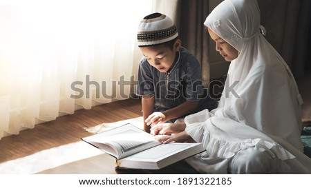 Religious Asian Muslim kids learn  the Quran and study Islam after pray to God at home .Sunset light shining through the window.Peaceful and Marvelous warm climate. 