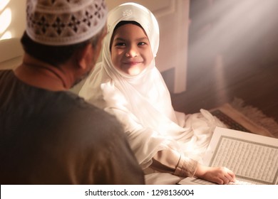 Religious Asian Muslim Man teaching his 6 years old daughter to learn the Quran and study Islam after pray to God at home .Sunset light shining through the window.Peaceful and Marvelous warm climate. 