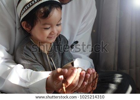 Religious Asian Muslim Man teaching his little son to pray to God with rosary at home.Sunset light shining through the window and touched boy body.Peaceful and Marvelous warm climate.Selective focus.