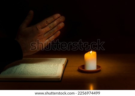 Religious concepts.The young payer prayed on the Bible in the room and lit the old candle to illuminate.Dark religion room.
