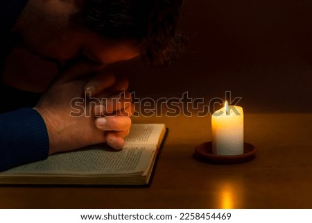 Religious concepts.The young payer prayed on the Bible in the room and lit the old candle to illuminate.Dark religion room.