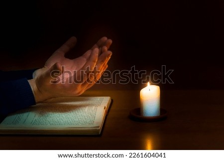 Religious concepts.The young payer prayed on the Bible in the room and lit the old candle to illuminate.Dark religion room.