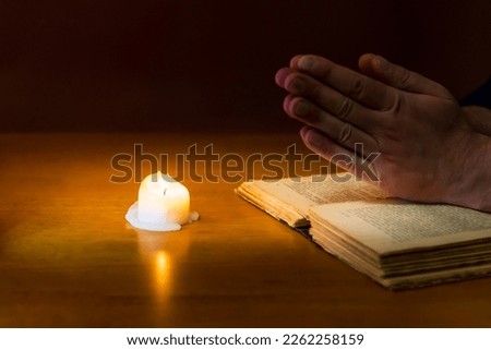 Religious concepts.The young payer prayed on the Bible in the room and lit the old candle to illuminate.Dark religion room.