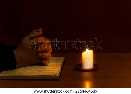 Religious concepts.The young payer prayed on the Bible in the room and lit the old candle to illuminate.Dark religion room.