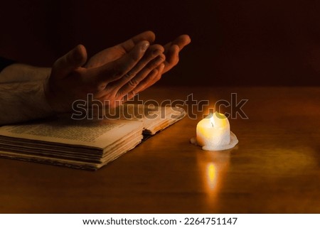 Religious concepts.The young payer prayed on the Bible in the room and lit the old candle to illuminate.Dark religion room.