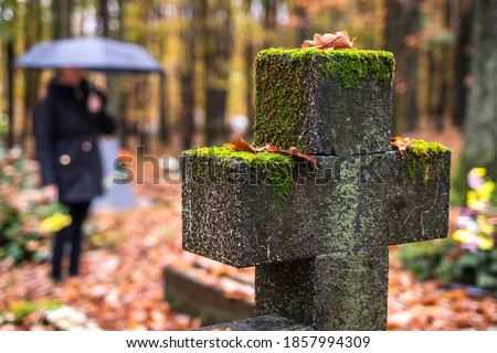 Religious cross in cemetery.  Mourning woman in black standing next to tombstone in rain.  Silent memory for dead relatives