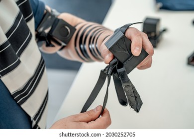 Religious jew, dressed in tallit and with tefillin on his left hand, holds a tefillin for his head. Jewish religious tradition