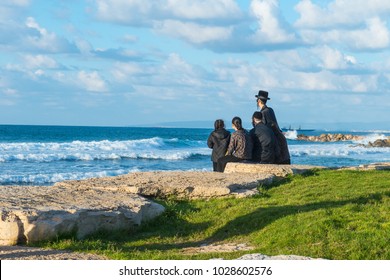 Religious Jew family sitting on the coast of Mediterranean sea in Israel and watching the waves. Sunset beach, family rest tradition. Selective focus, space for text