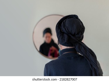Religious Jewish woman puts a shawl on her head in front of a mirror. Back view (27)