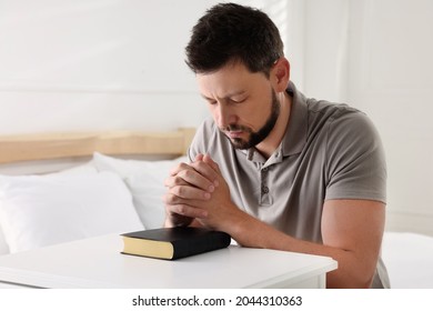 Religious man with Bible praying in bedroom