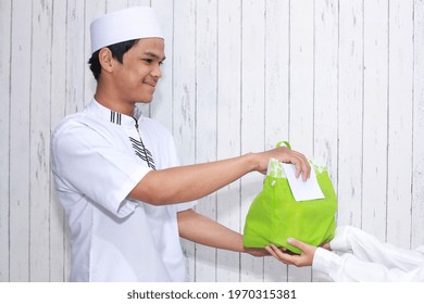 Religious Muslim Man Giving Alms In Form Of Food In A Green Bag And A White Envelope Filled With Money