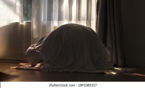 Religious Muslim young girl praying at home.Sunlight shining.Religious Asian Muslim lady  pray to God in Sujud poses.Pray iat home in morning or evening.