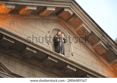 A religious statue of a robed saint holding the Christ child stands in an arched niche on the facade of a stone church building.