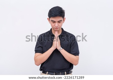 A religious young man in a black polo shirt closing his eyes and making a wish or praying. Isolated on a white backdrop.