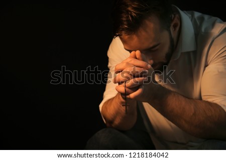 Religious young man praying to God on black background