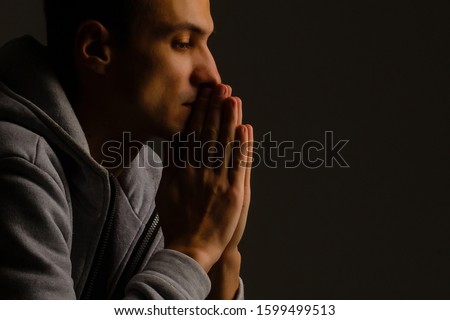 Religious young man praying to God on dark background, black and white effect