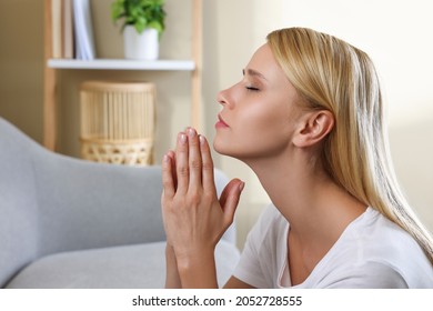 Religious young woman with clasped hands praying indoors. Space for text