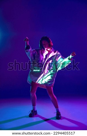 Reload. Portrait of girl, woman, wearing fashion clothes and dancing with emotion with inscription of neon glow on body over violet background. Concept of digital art, fashion, cyberpunk, futurism