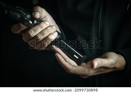 Reloading gun close-up. Man inserts drum of cartridges into pistol. Firearms in hand on dark background. Defense or attack.
