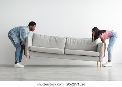 Relocation Concept. Portrait Of Smiling African American Couple Moving Sofa In New Apartment, Replacing Furniture At Home, Happy Black Man And Woman Placing Sofa In Cozy Studio Flat, Profile Side View