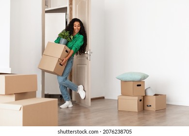 Relocation Concept. Portrait Of Young Lady Holding Pile Of Cardboard Boxes Walking In New House, Busy Person With Full Hands Moving Into Bought Apartment, Opens Door With Leg, Free Copy Space