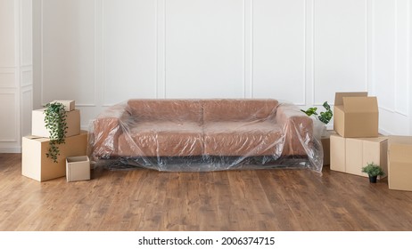 Relocation And Repair Concept. Modern Stylish Sofa Covered With Plastic Sheet For Home Decorating. Apartment Redecoration And Home Construction While Renovating And Improving Flat, Free Copy Space