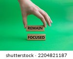 Remain focused symbol. Concept words Remain focused on wooden blocks. Beautiful green background. Businessman hand. Business and Remain focused concept. Copy space.