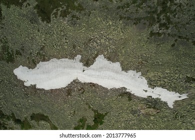 the remains of an avalanche in summer on the top of a volcano with a scattering of granite around a white spot
