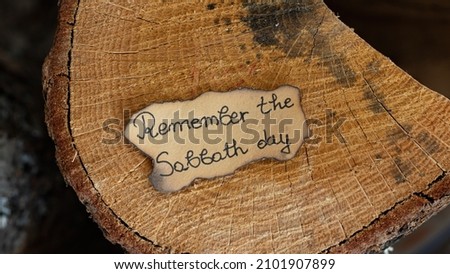 Remember the Sabbath Day text quote handwritten on old paper on an oak wooden log. Top overhead view. The biblical concept of rest, keeping the fourth commandment for Seventh Day Sabbath Holy.