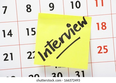 A reminder about an interview written on a yellow paper sticky note stuck to a wall calendar background