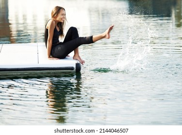 Reminiscing about her childhood years. A gorgeous young woman playfully kicking up water at the harbour. - Powered by Shutterstock