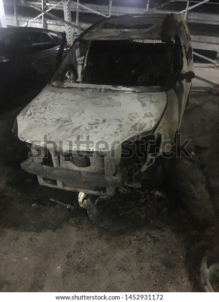 Remnants of a burnt car in a\
open garage. Insurance evidence and claim proof, low key, phone\
image