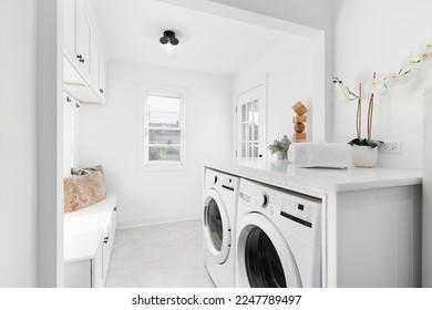 A remodeled laundry room and mud room with new appliances, tiled floor, and bench with cabinets above.