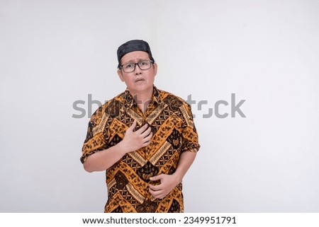 A remorseful man explains how he regrets his past actions. Asking for another chance. Wearing a batik shirt and songkok skull cap with hand on chest. Isolated on a white background.