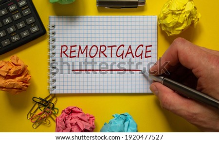 Remortgage symbol. Businessman writing word 'remortgage' on white note, beautiful yellow background, colored paper clips, metalic pen, cap and calculator. Business and remortgage concept.