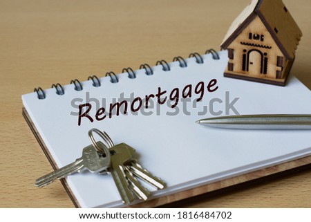 REMORTGAGE - the word is written in a notebook with a pen and a wooden house. Business and finance concept
