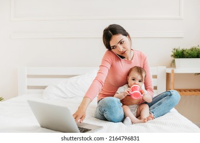 Remote Business. Busy Young Mom With Baby Working With Laptop And Smartphone At Home, Woman Using Laptop And Talking On Phone While Taking Care Of Baby, Free Space