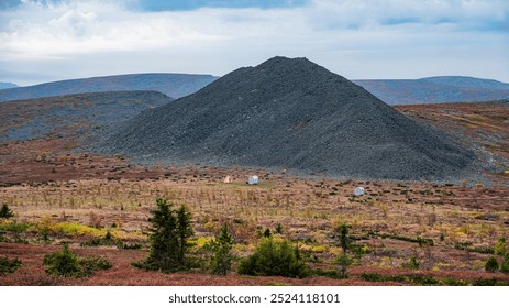 Remote campsite with a tent and hut sits in a vast open landscape near a rocky mountain under a cloudy sky.  - Powered by Shutterstock