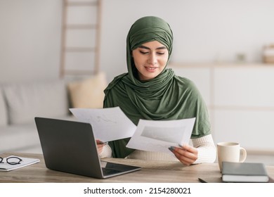 Remote career, freelance job, distance communication concept. Happy young Arab woman in hijab using laptop computer, looking through business documents during online work meeting at home - Powered by Shutterstock