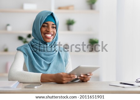 Remote Career. Portrait Of Happy Black Muslim Freelancer Lady With Digital Tablet Sitting At Desk In Home Office, Smiling African Islamic Woman In Hijab Using Tab Computer For Online Work
